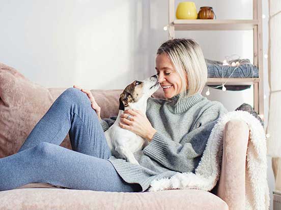 Smiling woman sitting on the sofa with dog on her lap