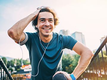 Man wearing headphones and smart watch, smiling and resting during run