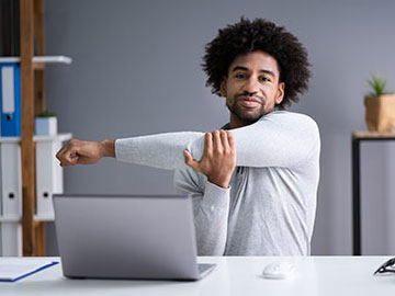 Man stretching his arm whilst sat at a desk