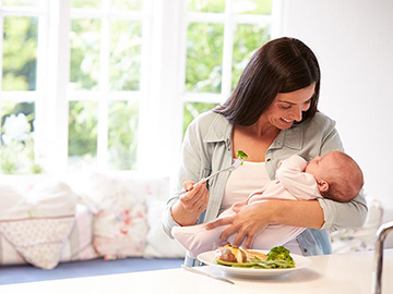 Woman eating healthy meal whilst holding baby