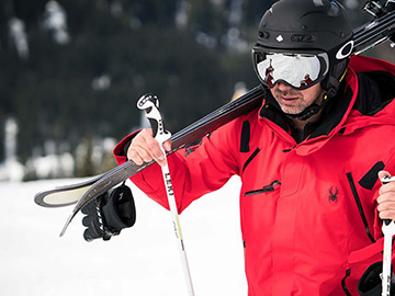 Man carrying a pair of skis on ski slope